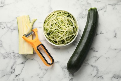Photo of Raw zucchini noodles, peeler and fresh vegetables on white marble table, flat lay. Vegetarian dish