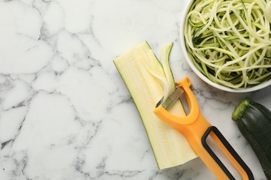 Photo of Vegetarian dish. Raw zucchini noodles, peeler and fresh vegetables on white marble table, flat lay. Space for text
