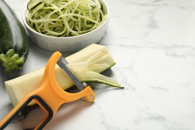 Photo of Vegetarian dish. Raw zucchini noodles, peeler and fresh vegetables on white marble table, closeup. Space for text