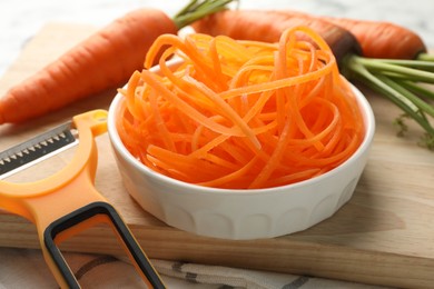 Photo of Raw carrot noodles, peeler and fresh vegetables on table, closeup. Vegetarian dish
