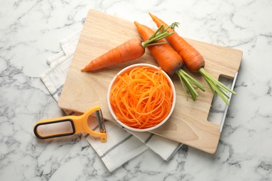 Photo of Raw carrot noodles, peeler and fresh vegetables on white marble table, flat lay. Vegetarian dish