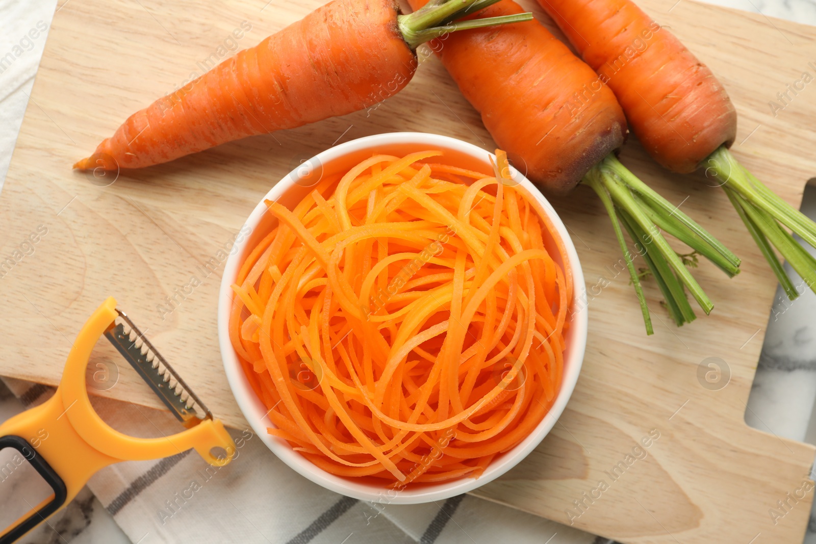 Raw carrot noodles, peeler and fresh vegetables on table, flat lay. Vegetarian dish Photo of Raw carrot noodles, peeler and fresh vegetables on table, flat lay. Vegetarian dish