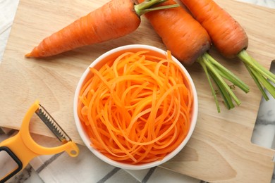 Photo of Raw carrot noodles, peeler and fresh vegetables on table, flat lay. Vegetarian dish