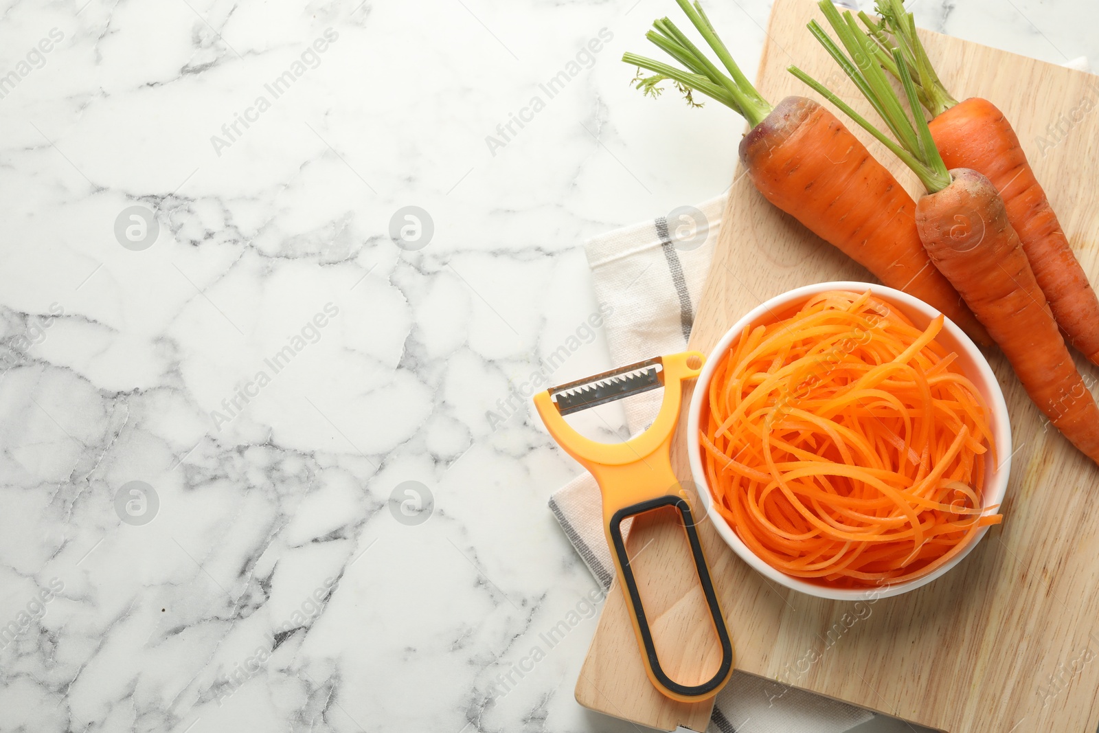 Photo of Vegetarian dish. Raw carrot noodles, peeler and fresh vegetables on white marble table, flat lay. Space for text