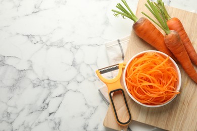 Photo of Vegetarian dish. Raw carrot noodles, peeler and fresh vegetables on white marble table, flat lay. Space for text