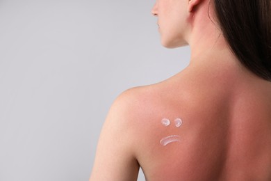 Photo of Woman with sun protection product on her sunburned skin against grey background, closeup. Space for text