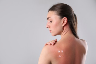 Photo of Woman with sun protection product on her sunburned skin against grey background, space for text