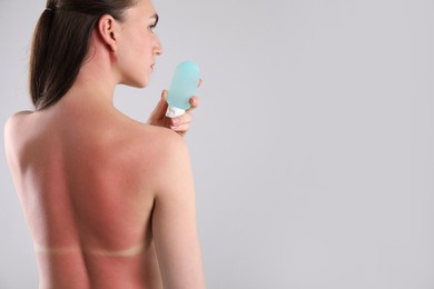 Photo of Woman with sunburned skin holding bottle of sun protection product on grey background, back view. Space for text
