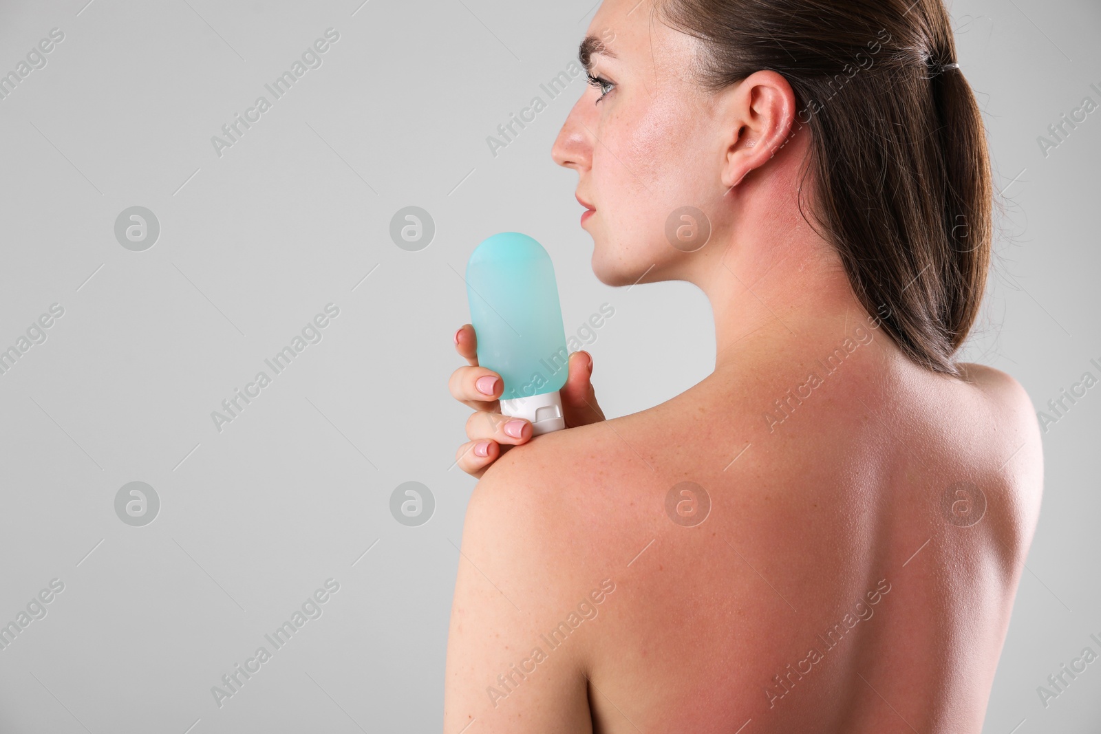 Woman with sunburned skin holding bottle of sun protection product on grey background, space for text Photo of Woman with sunburned skin holding bottle of sun protection product on grey background, space for text
