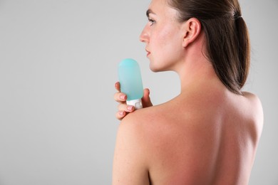 Photo of Woman with sunburned skin holding bottle of sun protection product on grey background, space for text