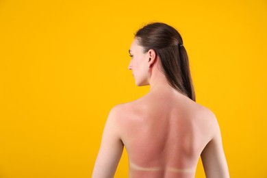 Photo of Woman with sunburned skin on orange background, back view. Space for text