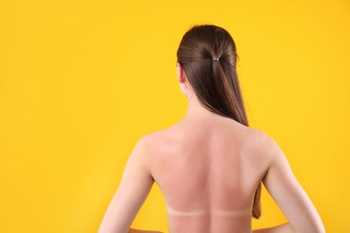 Photo of Woman with sunburned skin on orange background, back view. Space for text
