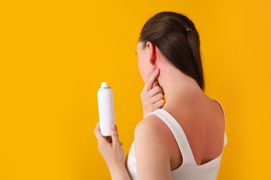 Photo of Woman with sunburned skin holding bottle of sun protection product on orange background, space for text