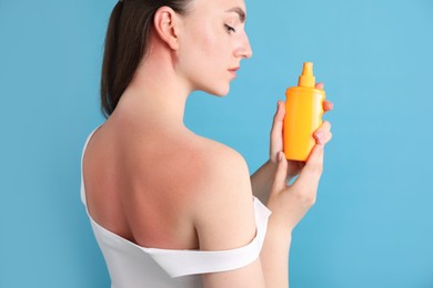Photo of Woman with sunburned skin holding bottle of sun protection product on light blue background
