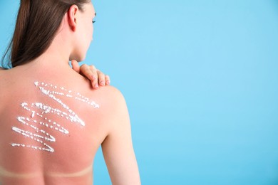 Photo of Woman with sun protection product on her sunburned skin against light blue background, back view. Space for text