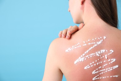 Photo of Woman with sun protection product on her sunburned skin against light blue background, back view. Space for text