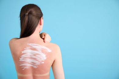 Photo of Woman with sun protection product on her sunburned skin against light blue background, back view. Space for text
