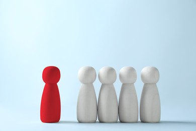 Image of Dismissal. Red figure standing apart among wooden ones on light background