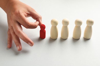Image of Dismissal. Woman choosing red figure among wooden ones at white table, closeup