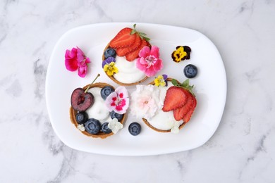 Photo of Sweet tartlets with berries and flowers on light marble table, top view. Delicious dessert