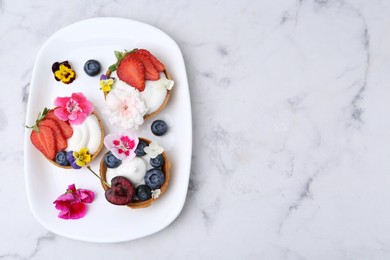 Photo of Sweet tartlets with berries and flowers on light marble table, top view with space for text. Delicious dessert