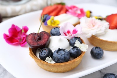 Photo of Sweet tartlets with berries and flowers on light table, closeup. Delicious dessert