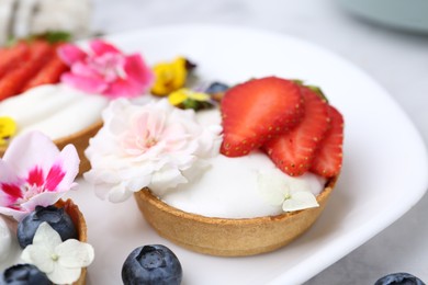 Photo of Sweet tartlets with berries and flowers on light table, closeup. Delicious dessert