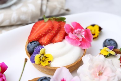 Photo of Sweet tartlets with berries and flowers on light table, closeup. Delicious dessert