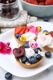 Photo of Sweet tartlets with berries and flowers on light marble table, closeup. Delicious dessert