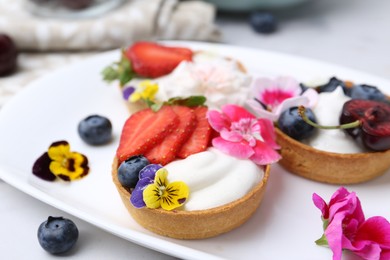 Photo of Sweet tartlets with berries and flowers on light table, closeup. Delicious dessert