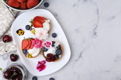 Photo of Sweet tartlets with berries and flowers on light marble table, flat lay with space for text. Delicious dessert