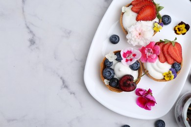 Photo of Sweet tartlets with berries and flowers on light marble table, flat lay with space for text. Delicious dessert