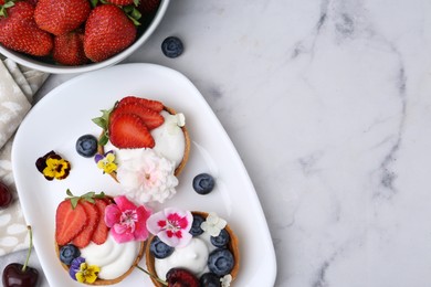 Photo of Sweet tartlets with berries and flowers on light marble table, flat lay with space for text. Delicious dessert