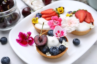 Photo of Sweet tartlets with berries and flowers on light table, closeup. Delicious dessert