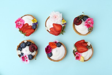 Photo of Sweet tartlets with berries and flowers on turquoise background, flat lay. Delicious dessert