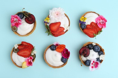 Photo of Sweet tartlets with berries and flowers on turquoise background, flat lay. Delicious dessert
