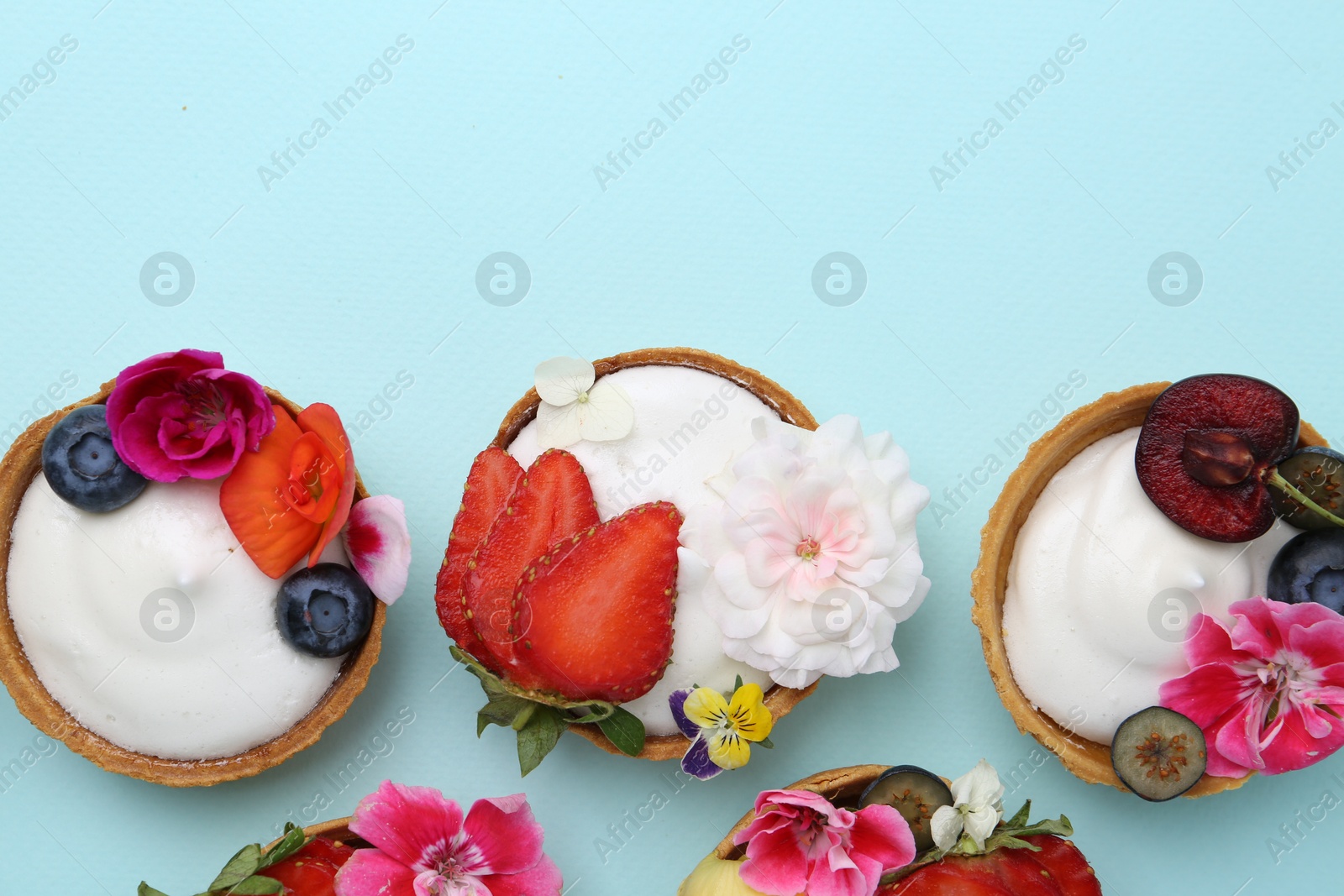 Sweet tartlets with berries and flowers on turquoise background, flat lay with space for text. Delicious dessert Photo of Sweet tartlets with berries and flowers on turquoise background, flat lay with space for text. Delicious dessert