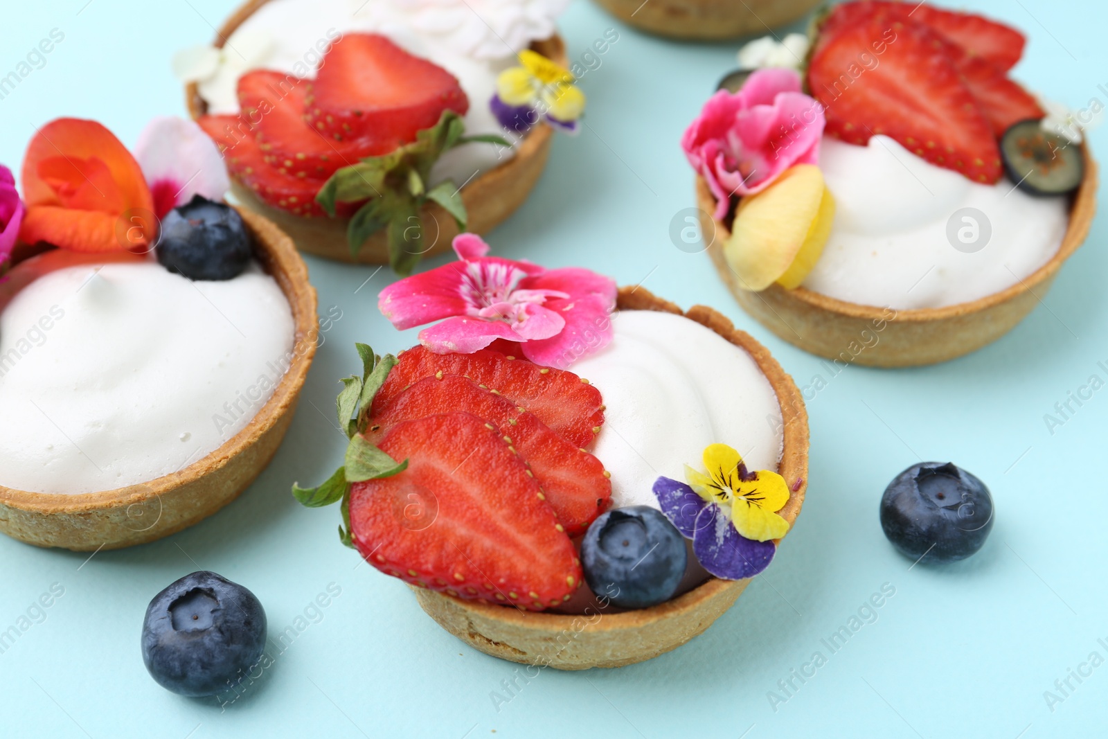 Sweet tartlets with berries and flowers on turquoise background, closeup. Delicious dessert Photo of Sweet tartlets with berries and flowers on turquoise background, closeup. Delicious dessert