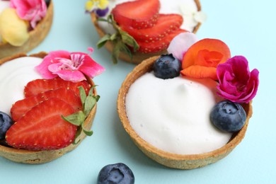 Photo of Sweet tartlets with berries and flowers on turquoise background, closeup. Delicious dessert