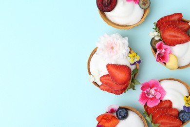 Photo of Sweet tartlets with berries and flowers on turquoise background, flat lay with space for text. Delicious dessert