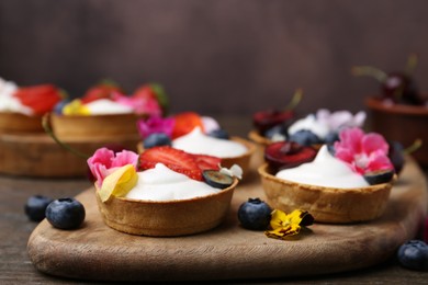 Photo of Sweet tartlets with berries and flowers on wooden table against brown background, closeup. Delicious dessert