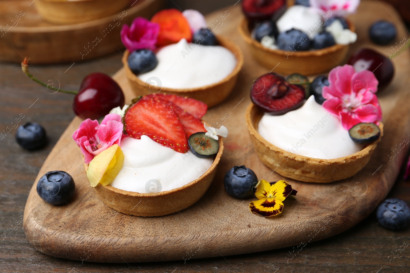 Sweet tartlets with berries and flowers on wooden table, closeup. Delicious dessert Photo of Sweet tartlets with berries and flowers on wooden table, closeup. Delicious dessert