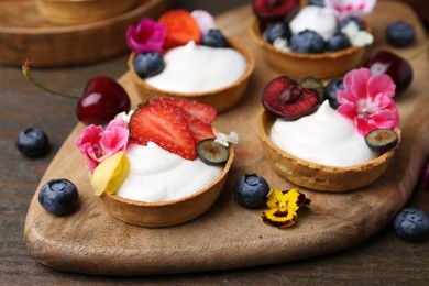 Photo of Sweet tartlets with berries and flowers on wooden table, closeup. Delicious dessert