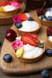 Photo of Sweet tartlets with berries and flowers on wooden table, closeup. Delicious dessert