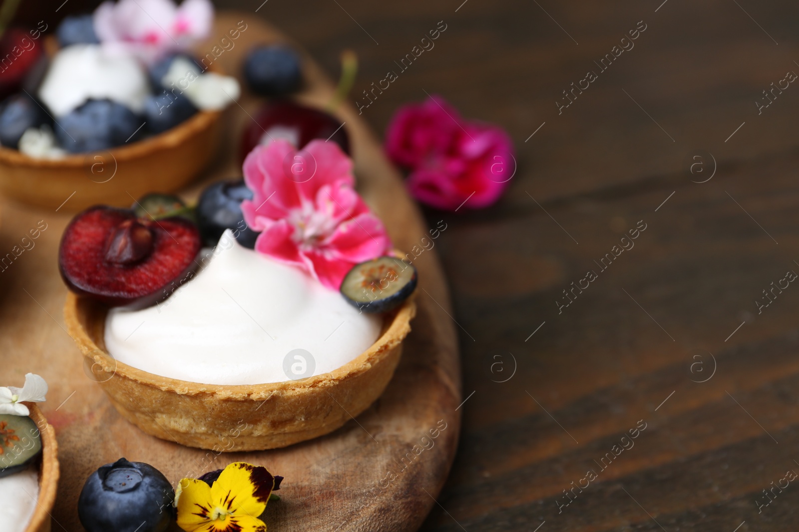 Sweet tartlets with berries and flowers on wooden table, closeup with space for text. Delicious dessert Photo of Sweet tartlets with berries and flowers on wooden table, closeup with space for text. Delicious dessert