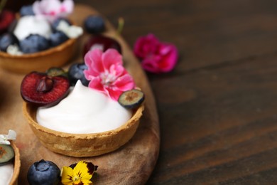 Photo of Sweet tartlets with berries and flowers on wooden table, closeup with space for text. Delicious dessert