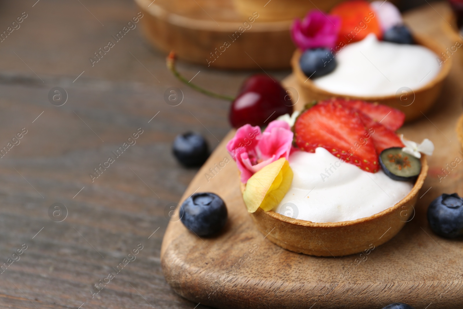 Sweet tartlets with berries and flowers on wooden table, closeup with space for text. Delicious dessert Photo of Sweet tartlets with berries and flowers on wooden table, closeup with space for text. Delicious dessert