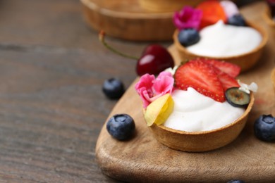 Photo of Sweet tartlets with berries and flowers on wooden table, closeup with space for text. Delicious dessert