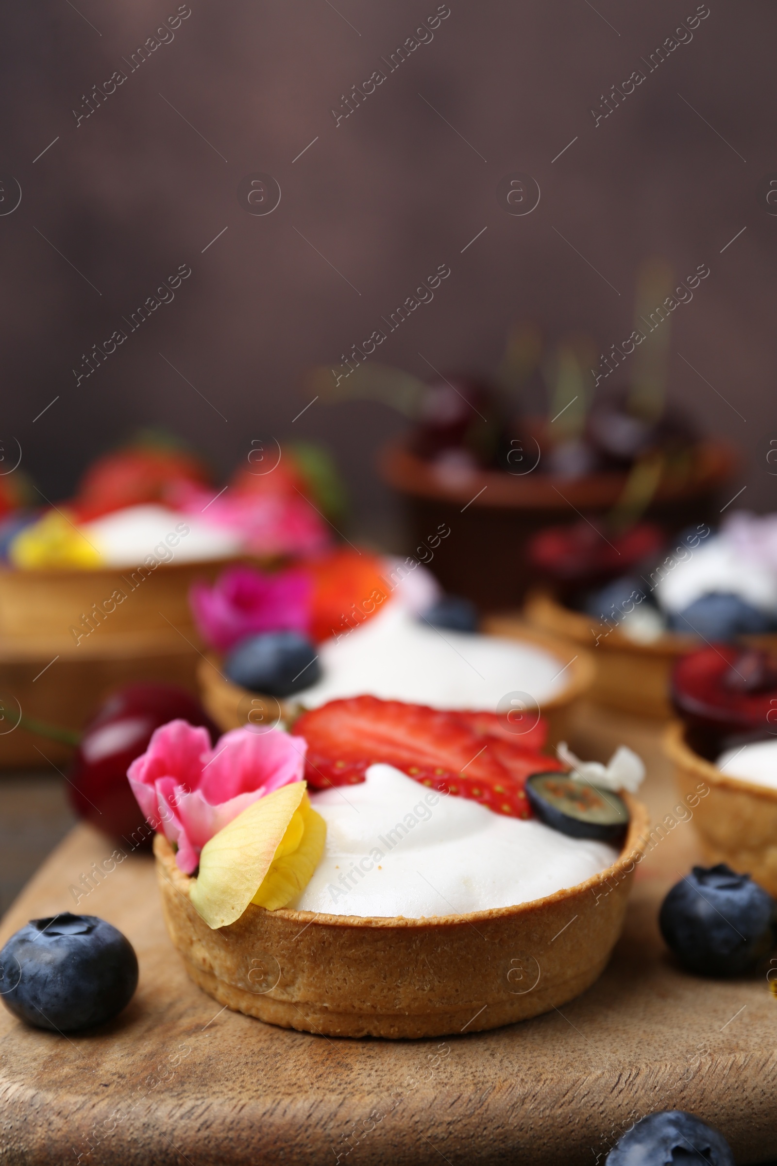 Photo of Sweet tartlets with berries and flowers on table against brown background, closeup. Delicious dessert