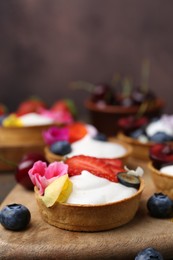 Photo of Sweet tartlets with berries and flowers on table against brown background, closeup. Delicious dessert